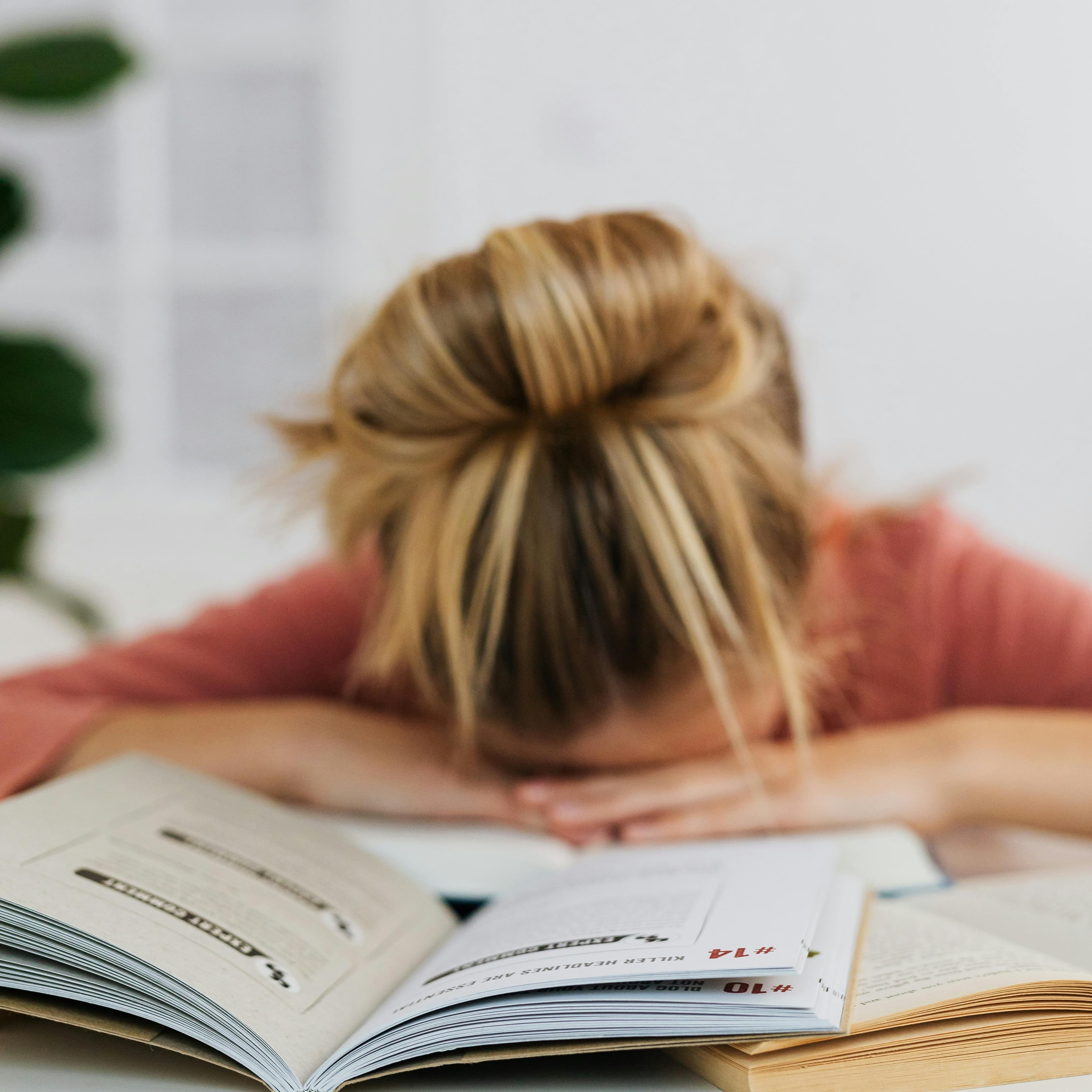 School-age girl with head in a top knot has her head resting on her hands on a desk with open books