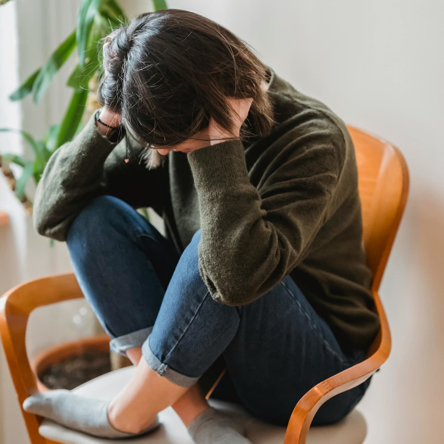 Teen sitting cross-legged on a chair with their head in their hands and knees pulled in