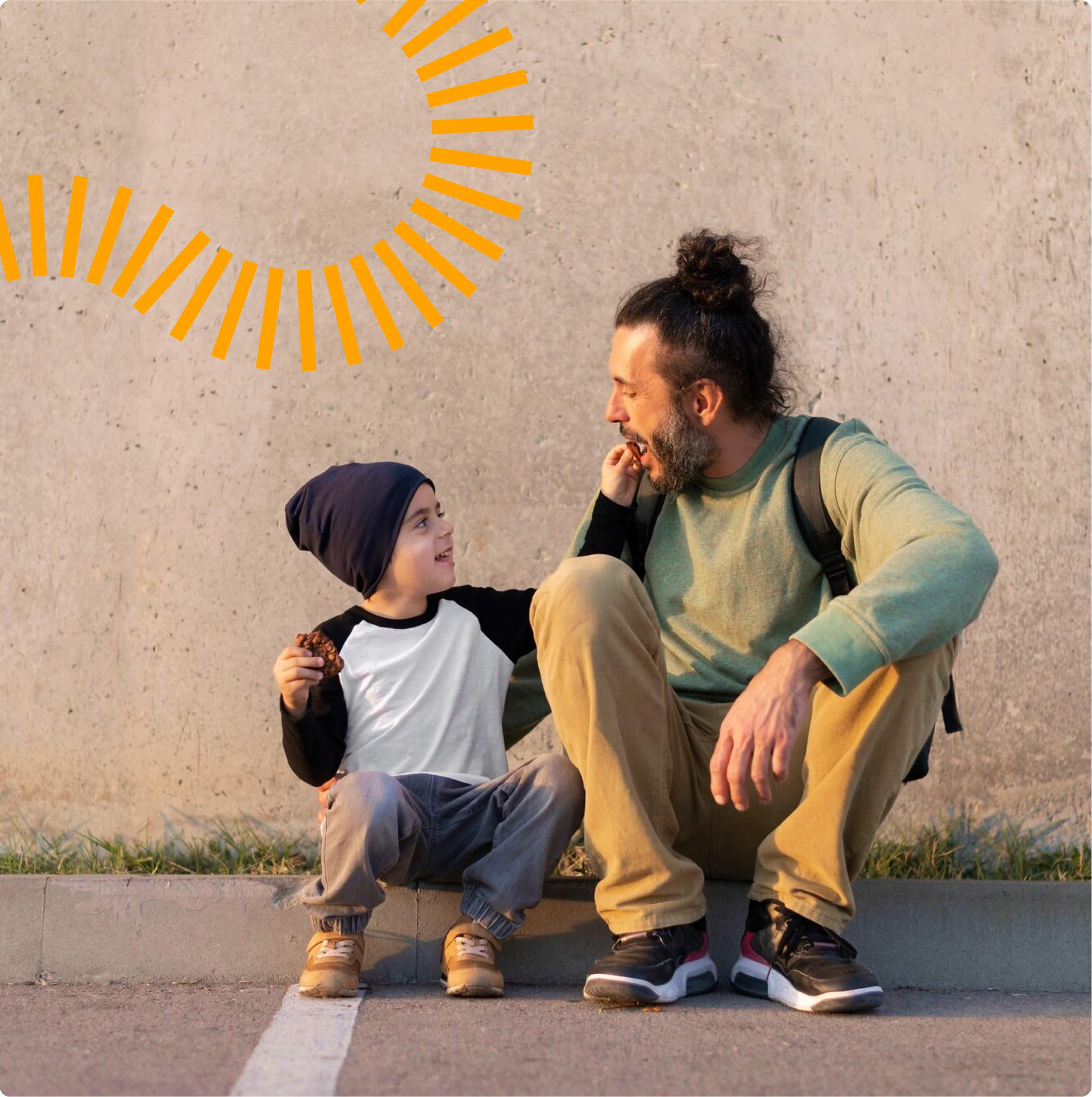 A tender moment between an adult and child sitting together on a concrete ledge against a beige wall with orange sun decoration. The adult wears a mint green sweater and khakis, while the child wears a beanie, baseball-style shirt, and holds what appears to be a snack. They're sharing a joyful conversation outdoors.