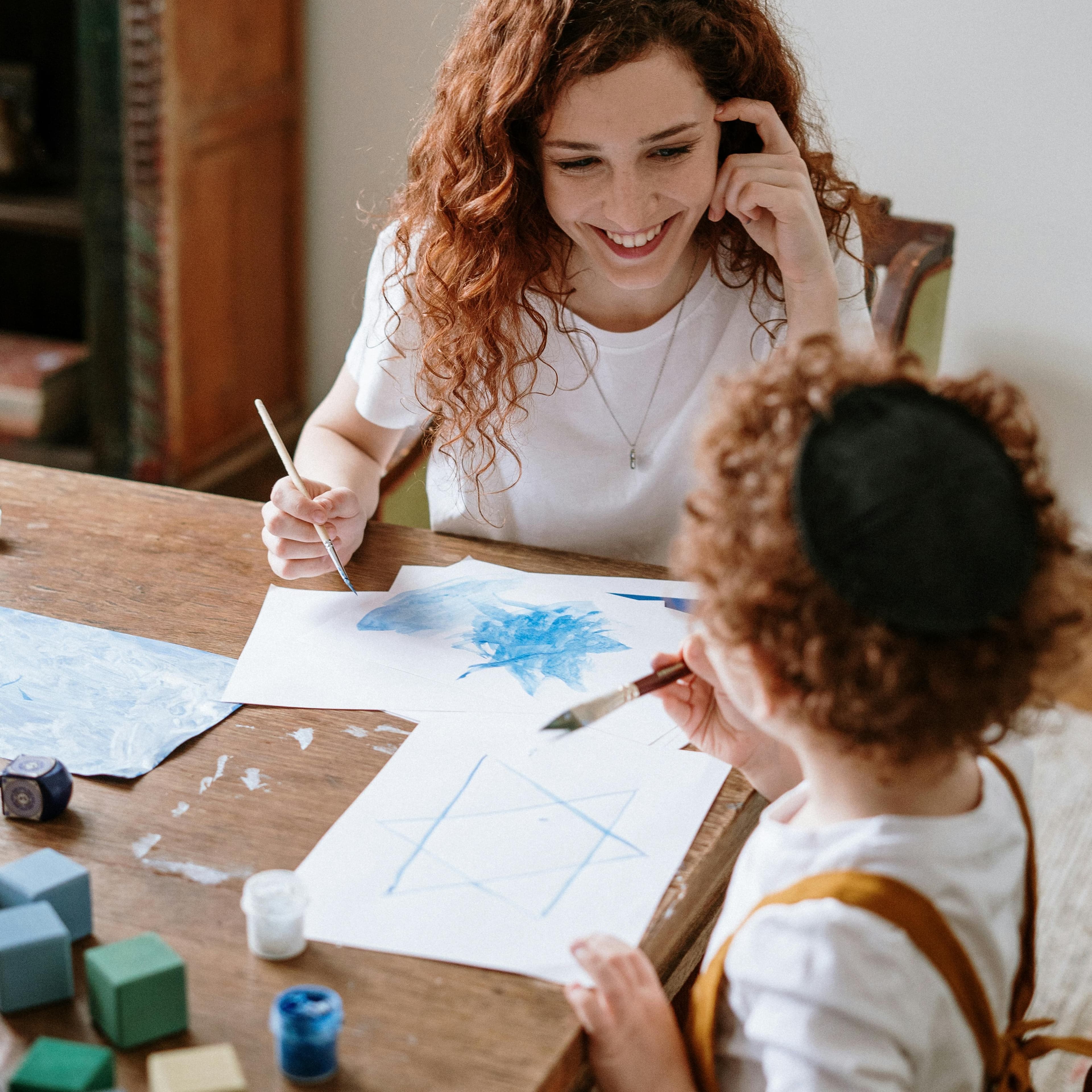 Mother smiling at her young son sitting together at a table doing Hanukkah crafts