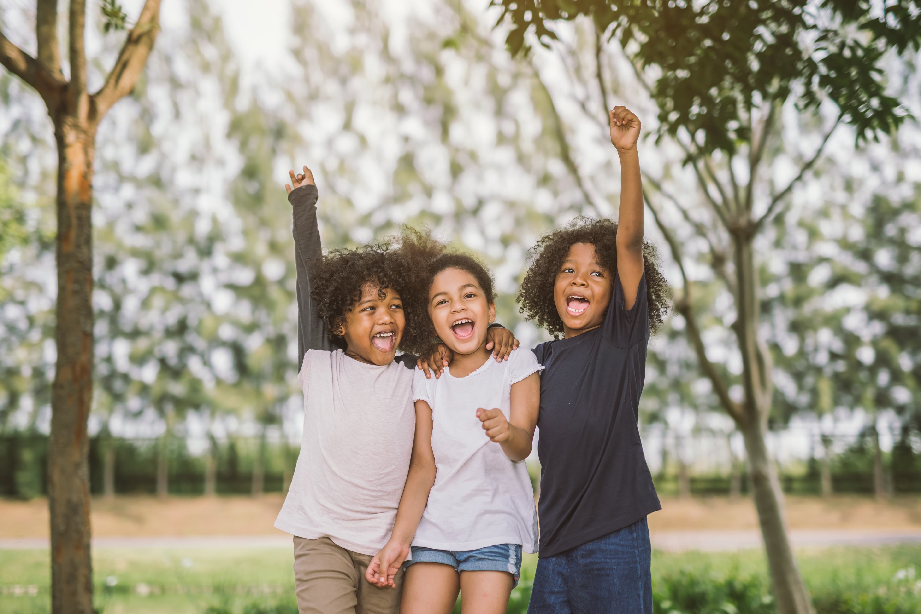 Three younger kids active, cheering, hugging and enjoying being outside