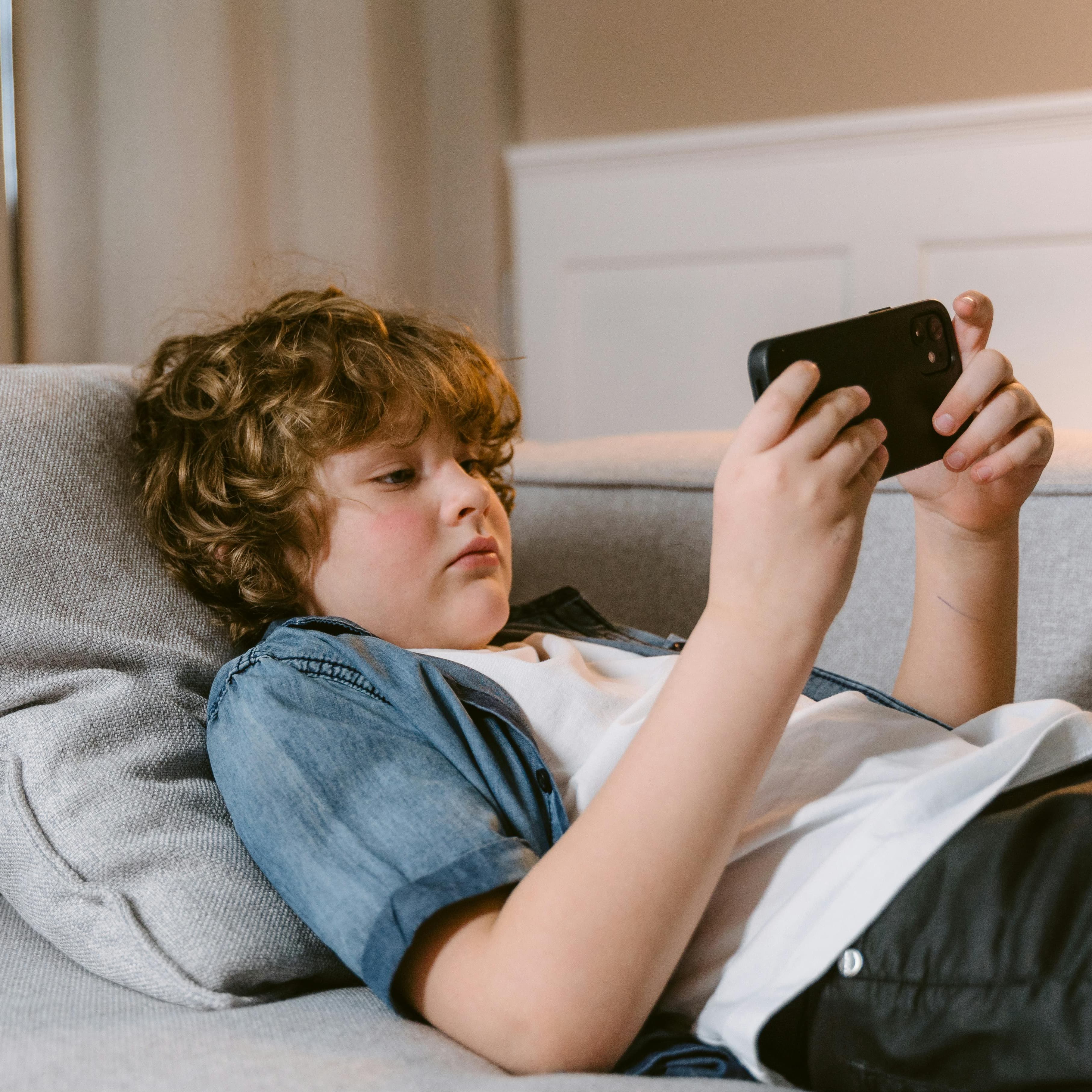 Young boy laying on couch looking at his phone