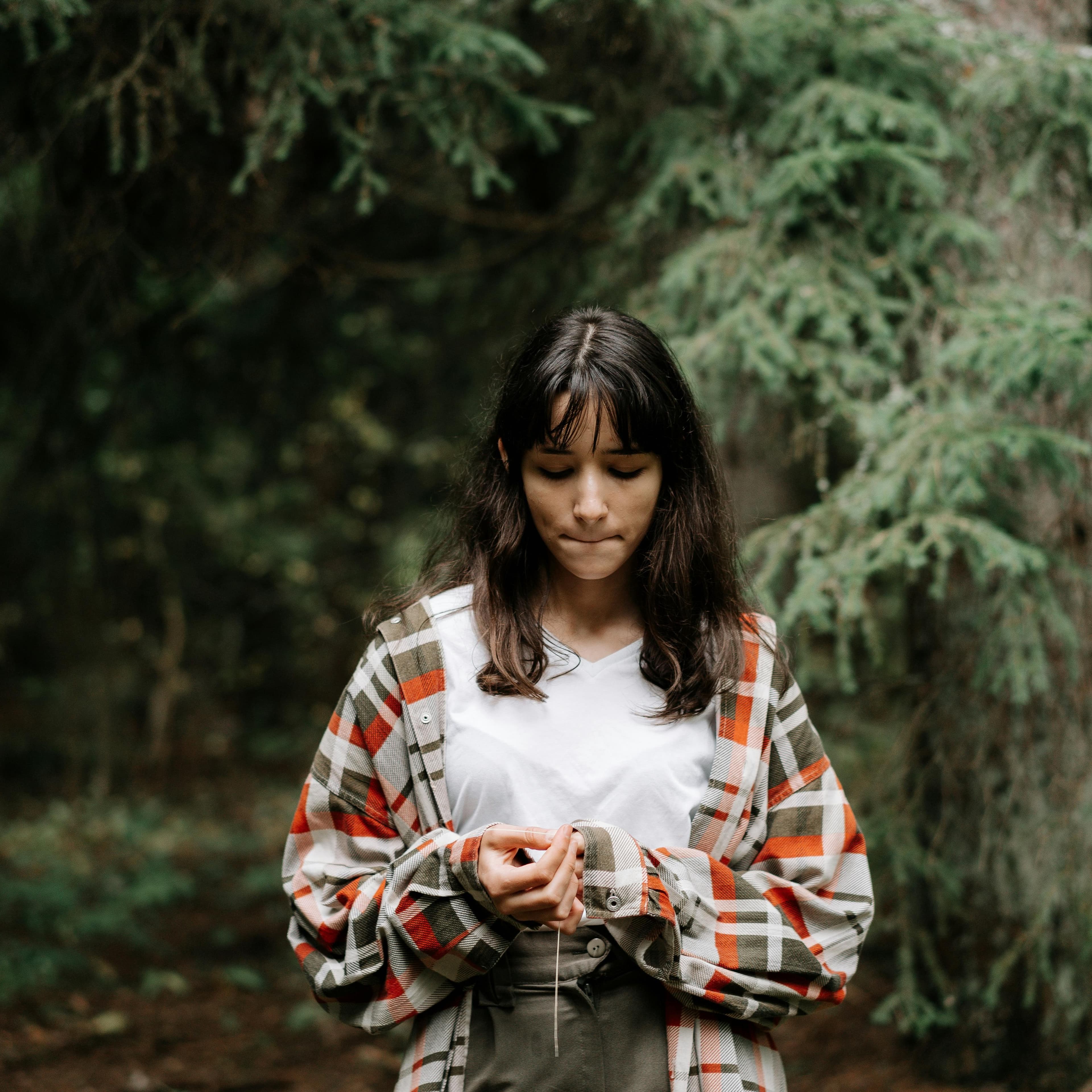 Teenage girl standing in the woods wearing loose flannel shirt and looking down at her hands