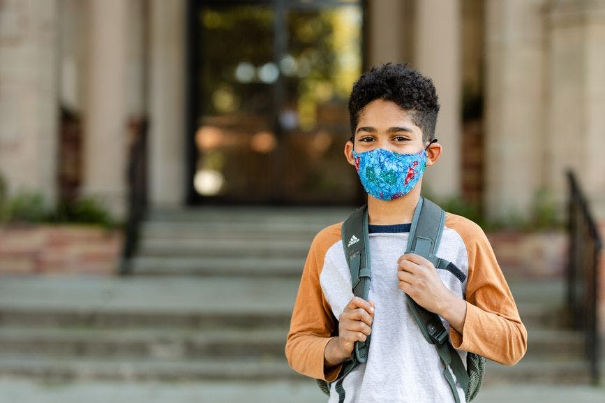 boy wearing mask outside school with backpack on