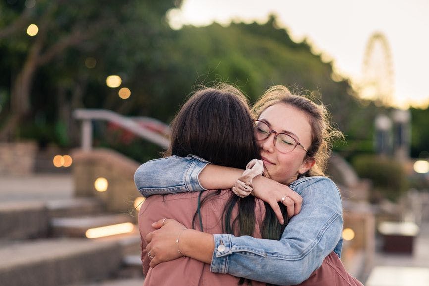two teenage girls hugging outside