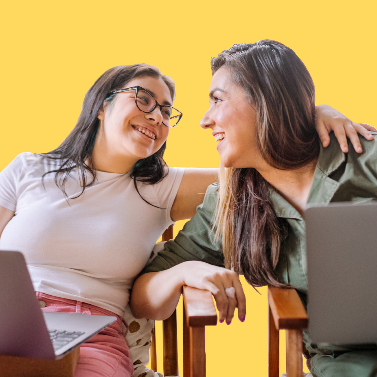 Teenage girl and mom with laptops laughing together, girl's arm around her mother